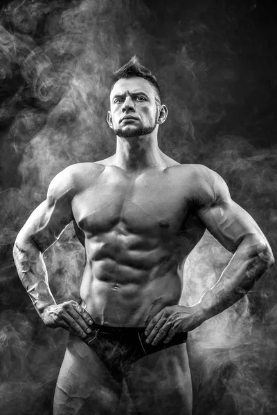 Stilig power atletisk man bodybuilder. Konditionen muskulös kropp på mörk rök bakgrund. Perfekta hane. Awesome bodybuilder, poserar. — Stockfoto