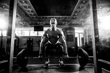 Genç üstsüz adam spor salonunda kaldırma egzersizi yapıyor. Motivasyon için çığlık atmak