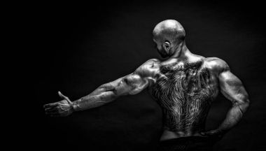 Arkadan görünüşü tattoed vücut geliştirmeci uzanmış kolu