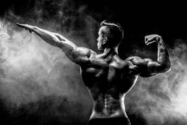 Visão traseira do homem irreconhecível, músculos fortes posando com o braço para cima na fumaça . — Fotografia de Stock