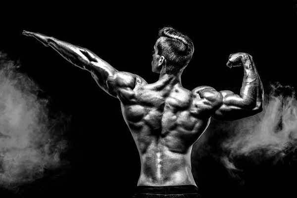 Back view of Unrecognizable man, strong muscles posing with arm up in smoke.