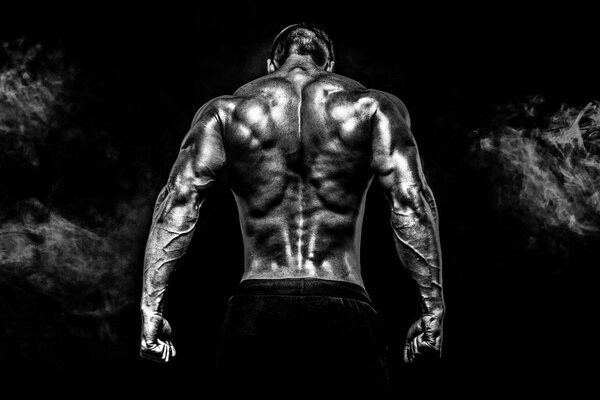 Back view of Unrecognizable man, strong muscles posing with arm up in smoke.