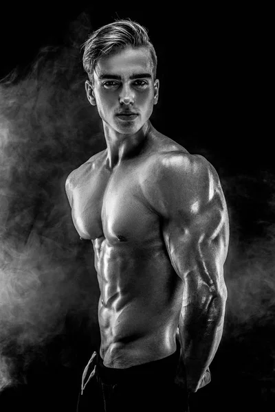 Forte bodybuilder uomo con addominali perfetti, spalle, bicipiti, tricipiti, petto in posa in fumo . — Foto Stock