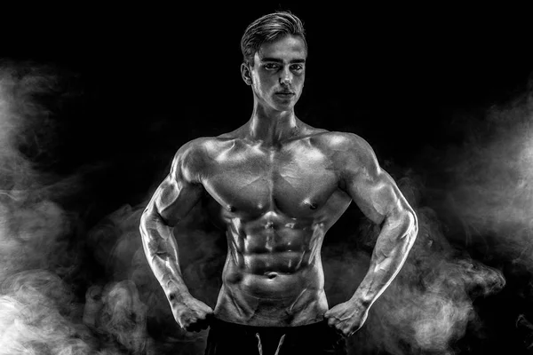Ισχυρή bodybuilder άνδρας με τέλειους κοιλιακούς, ώμους, δικέφαλου, τρικέφαλοι, στήθος ποζάρει στον καπνό. — Φωτογραφία Αρχείου