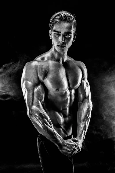 Hombre fuerte culturista con abdominales perfectos, hombros, bíceps, tríceps, pecho posando en el humo . — Foto de Stock