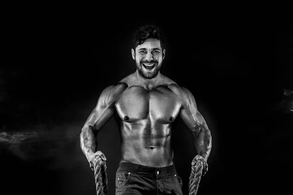 Hombre musculoso sosteniendo la cuerda y posando sobre el fondo negro con humo rojo — Foto de Stock