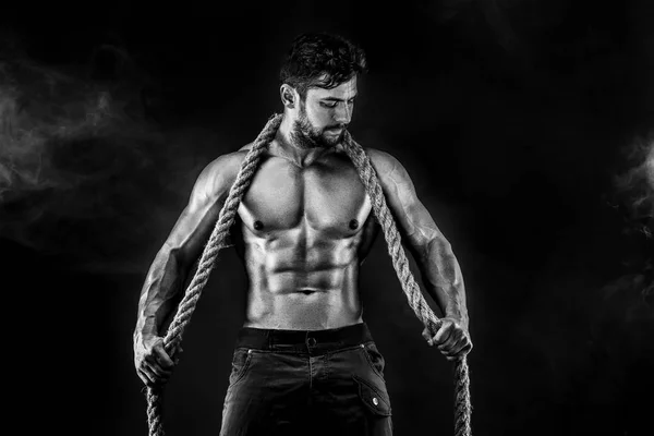 Homem muscular segurando corda e posando no fundo preto com fumaça vermelha — Fotografia de Stock