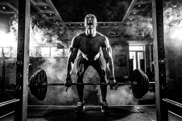 Un joven sin camisa haciendo ejercicio en el gimnasio. Gritando por motivación — Foto de Stock