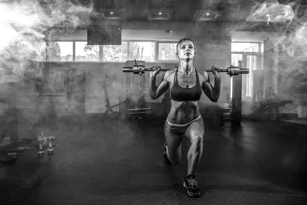 Jeune fille sexy dans la salle de gym faire squat sur fond de fumée — Photo