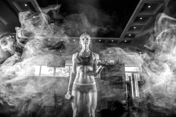 Sexy athlete blonde fitness woman in the gym workout with dumb on bicep. smoke — Stock Photo, Image