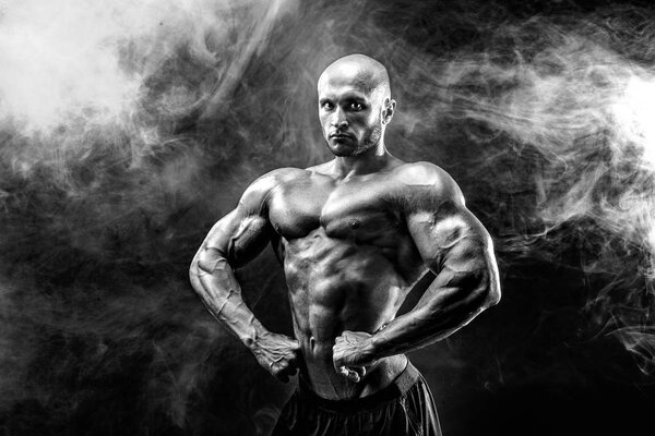 Strong bald bodybuilder with six pack. Bodybuilder man with perfect abs, shoulders,biceps, triceps and chest, personal fitness trainer flexing his muscles in blue, red smoke