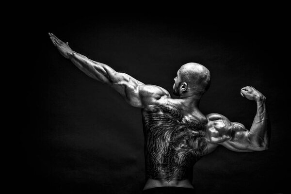 Back view of tattoed bodybuilder with outstretched arms