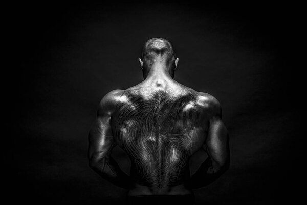 Back view of tattoed bodybuilder with outstretched arms