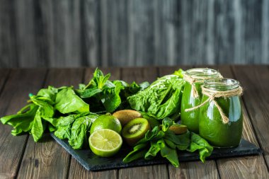 Taş tahtadaki malzemelerle harmanlanmış yeşil smoothie, ahşap masa seçici odak