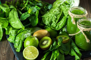 Taş tahtadaki malzemelerle harmanlanmış yeşil smoothie, ahşap masa seçici odak