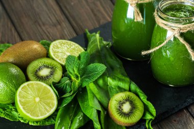 Taş tahtadaki malzemelerle harmanlanmış yeşil smoothie, ahşap masa seçici odak