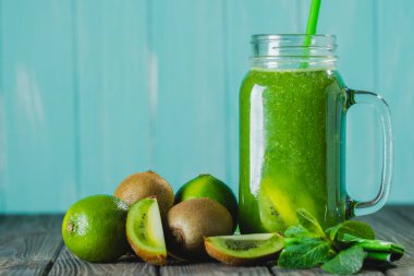 Malzemelerin üzerine ahşap masa seçici odak ile karıştırılmış yeşil güler yüzlü. Mavi arka plan.