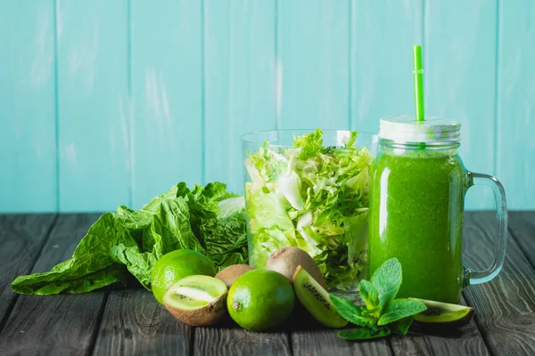 Batido verde mezclado con ingredientes en la mesa de madera enfoque selectivo. Fondo azul . —  Fotos de Stock