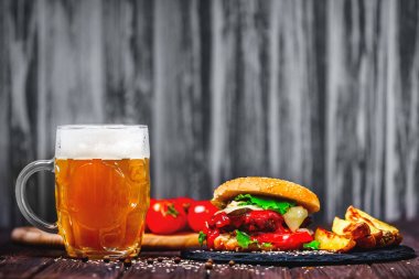 Ev yapımı lezzetli, ağız sulandıran sığır eti burger marul ve patates, taş kesme tahtası üzerinde bardak bira servis. Ahşap arka plan