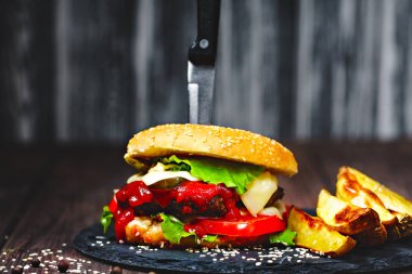 Bir bıçak ile ağız sulandıran, lezzetli ev yapımı hamburger closeup taş tahtaya sıkışmış. Koyu ahşap arka plan