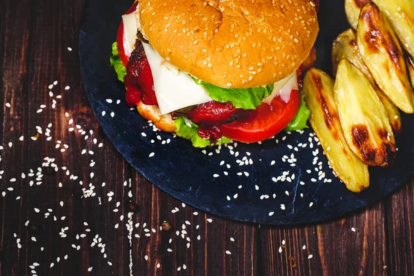Closeup of home made beef burger with lettuce and potato served on stone cutting board. Dark wooden background — Stock Photo, Image