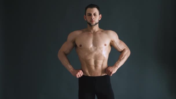 Bodybuilder fléchissant ses muscles en studio, fond gris foncé — Video