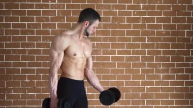 Pazı egzersiz dumbbells ile tuğla duvarın üzerinden performans konsantre üstsüz vücut geliştirmeci.