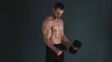Pazı egzersiz dumbbells ile gri arka plan üzerinde performans üstsüz vücut geliştirmeci yoğunlaşmıştır. Ağır çekim