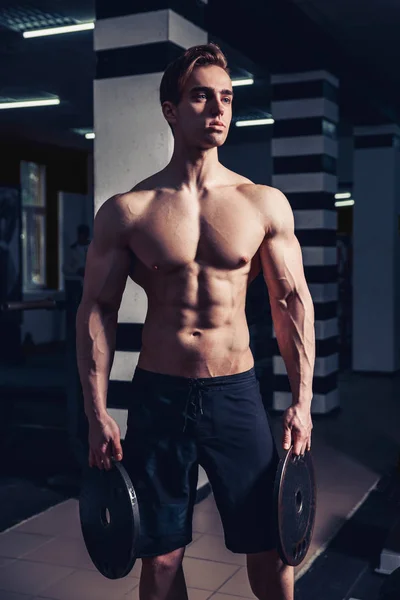 Sportler muskulöser Bodybuilder posiert mit Hanteln im Fitnessstudio. — Stockfoto