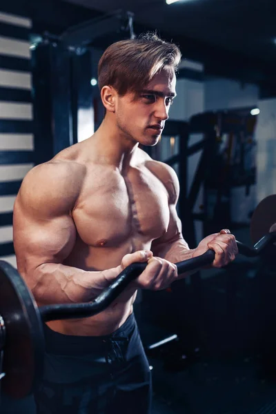 Musculoso culturista chico haciendo ejercicios en bíceps con gran mancuerna en el gimnasio —  Fotos de Stock