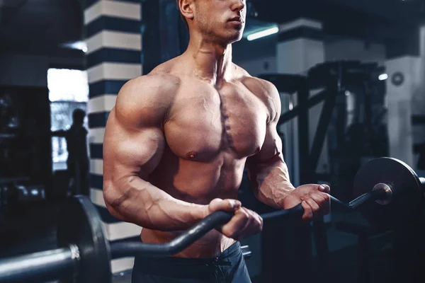 Musculoso culturista chico haciendo ejercicios en bíceps con gran mancuerna en el gimnasio —  Fotos de Stock