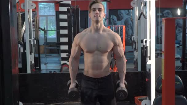 Gespierde bodybuilder man doen oefeningen op biceps met halters in sportschool — Stockvideo