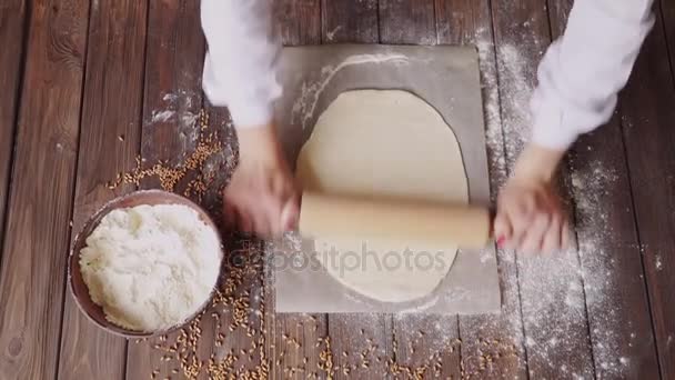 Mulher rolando massa em uma tábua de corte na mesa de madeira cheia de farinha na cozinha em casa . — Vídeo de Stock