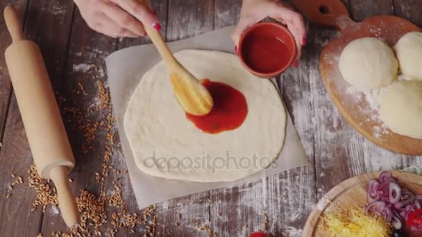 Vrouw zet saus op het deeg terwijl het maken van pizza in de keuken — Stockvideo