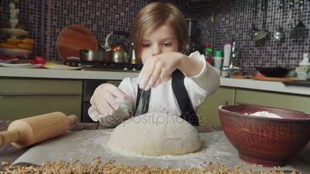 Filmagem de um belo lírio 5 anos de idade menina amassar a massa na mesa de madeira cheia de farinha na cozinha em casa . — Vídeo de Stock