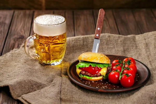 Hamburguesa de carne casera y verduras frescas en plato de arcilla con vaso de cerveza en la mesa de madera rústica, espacio de copia — Foto de Stock