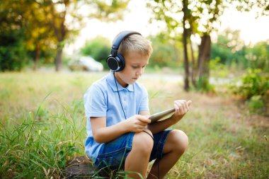 Ormandaki kulaklık giyen ve tablet üzerinde bir oyun oynarken oturan genç çocuk