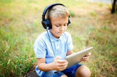 Ormandaki kulaklık giyen ve tablet üzerinde bir oyun oynarken oturan genç çocuk