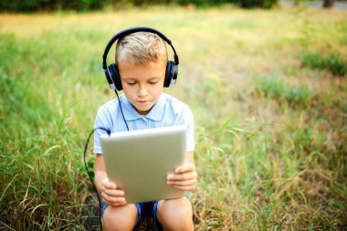 Ormandaki kulaklık giyen ve tablet üzerinde bir oyun oynarken oturan genç çocuk