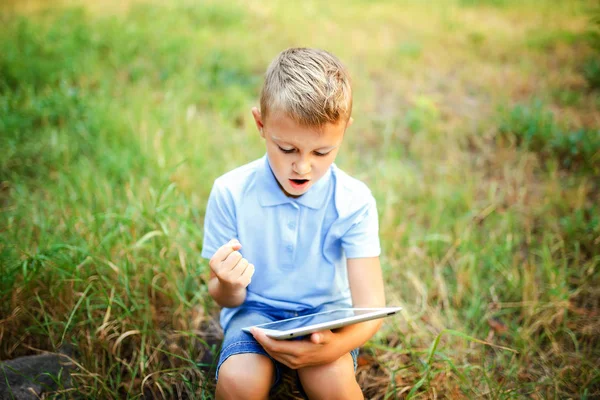 Młode dziecko sittingin dziedziniec i granie w gry na tablet — Zdjęcie stockowe