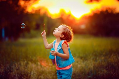 Beş yaşında çocuk kız sabun köpüğü günbatımında açık üfleme .