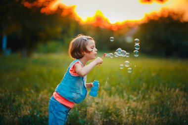 Beş yaşında çocuk kız sabun köpüğü günbatımında açık üfleme .