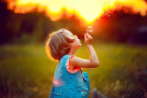 Cinco años de edad niña caucásica soplando burbujas de jabón al aire libre al atardecer  . — Foto de Stock