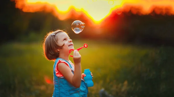 Cinco años de edad niña caucásica soplando burbujas de jabón al aire libre al atardecer  . — Foto de Stock
