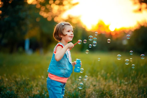 Cinco años de edad niña caucásica soplando burbujas de jabón al aire libre al atardecer  . — Foto de Stock