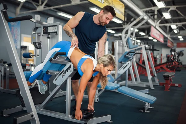 Sporty girl doing weight exercises with assistance of her personal trainer at gym. — Stock Photo, Image