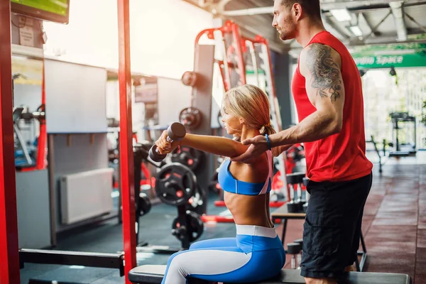 Sportliches Mädchen beim Krafttraining mit Unterstützung ihres Personal Trainers im Fitnessstudio. — Stockfoto