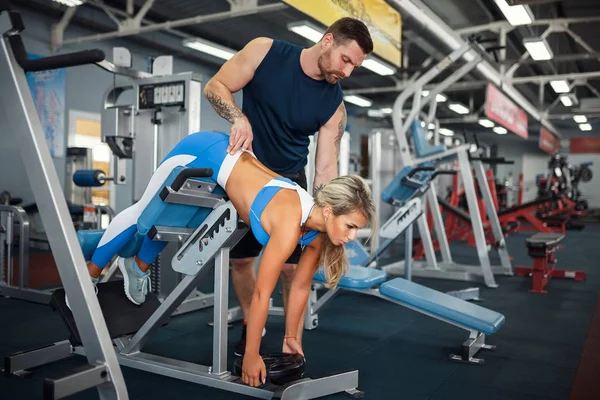 Sportig tjej gör vikt övningar med hjälp av hennes personliga tränare på gymmet. — Stockfoto