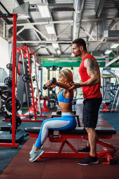 Sporty girl doing weight exercises with assistance of her personal trainer at gym. — Stock Photo, Image