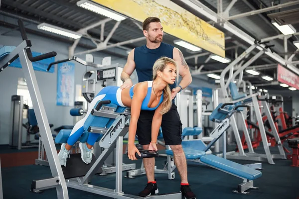 Sporty girl doing weight exercises with assistance of her personal trainer at gym. — Stock Photo, Image